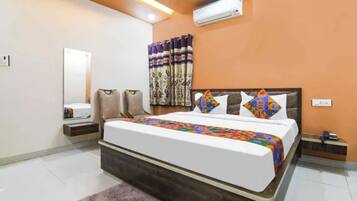 A hotel room with a bed, a nightstand, a mirror, and a wall-mounted air conditioner.