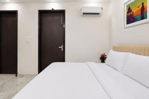 A hotel room with a bed, a door, an air conditioning unit, and a painting on the wall.