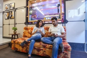 A man and a woman sitting on a sofa in a lobby area with framed artwork on the wall and a small table with a plant. - FabHotel Royal Palace Ab Road (Indore)
