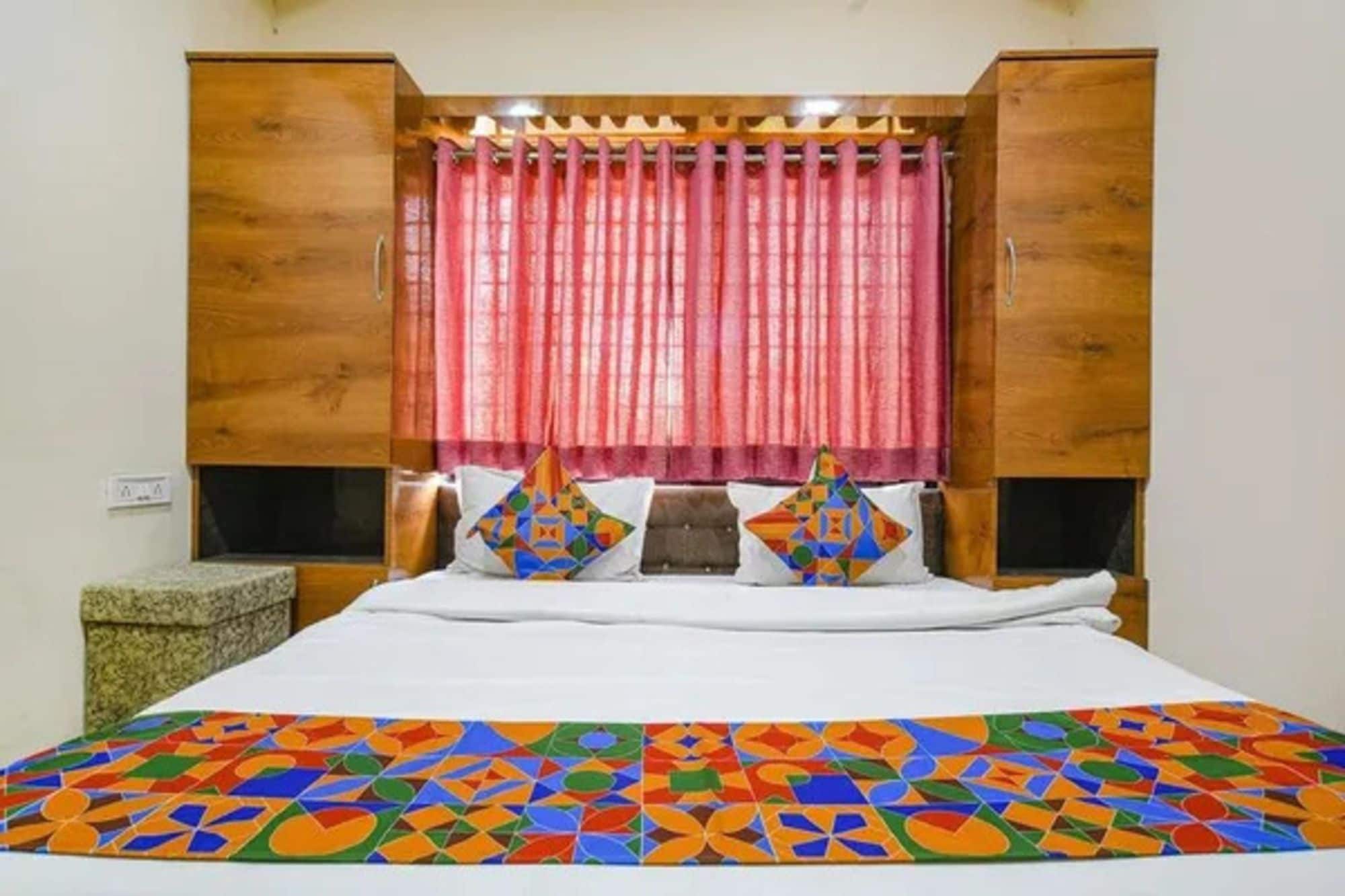 Un dormitorio con cabecera de madera, cama con colcha geométrica de colores y cortina rosa.