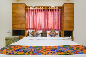 Quarto com cabeceira de madeira, cama com colcha geométrica colorida e cortina rosa.