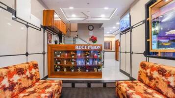 Zona de recepción con un mostrador de madera, un reloj y una escalera que conduce a un piso superior.