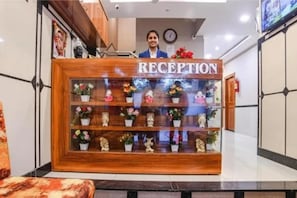 A reception desk with a wooden finish, a clock on the wall, and potted plants on the counter. - FabHotel Royal Palace Ab Road (Indore)