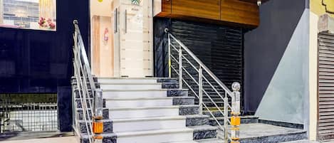 Una escalera con escalones de mármol y barandillas metálicas, que conduce a un techo de madera y un persiano negro cerrado.
