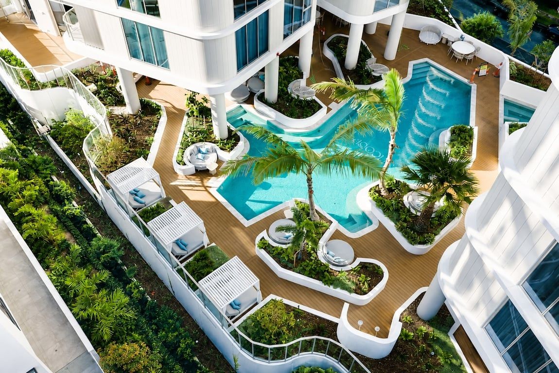 A multi-level hotel with a central swimming pool, outdoor seating areas, and lush landscaping.
