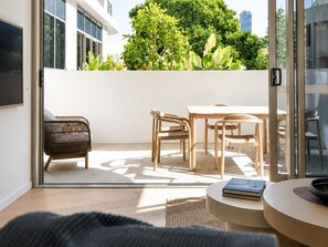 Ein modernes Interieur mit einer Glastür, die zu einem Außenbereich führt, einem runden Tisch mit Stühlen und einem Korbstuhl.