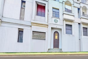 Un edificio de varios pisos con fachada plana, una entrada central con puerta y un pequeño balcón en el segundo piso.