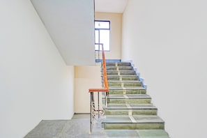 Una escalera con barandilla de metal y pasamanos de madera, que conduce a un rellano con una ventana.