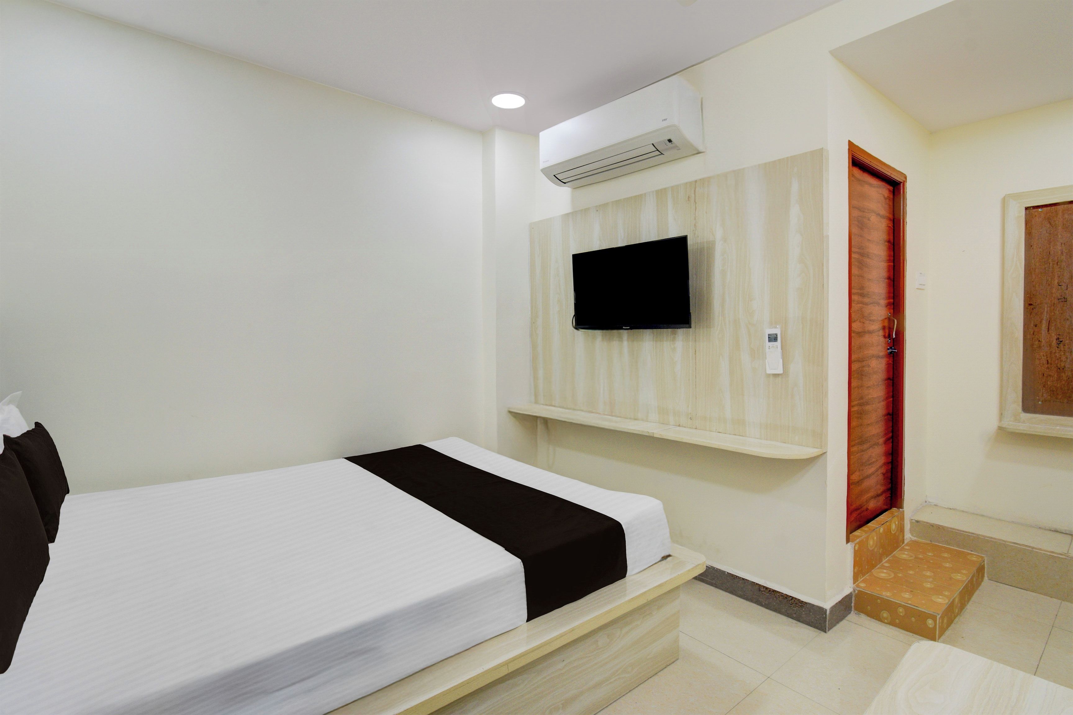 Habitación de hotel con una cama, televisor montado y una puerta de madera.