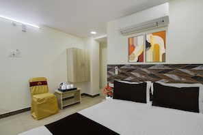 A hotel room with a bed, a chair, a small table with a coffee maker, a wardrobe, and a wall-mounted air conditioner. - Hotel O Saibaba Temple Chintal (Hyderabad)