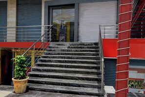 Un conjunto de escaleras de mármol negro que conducen a la entrada de un edificio, con una puerta de cristal, un toldo rojo y una barandilla de metal.