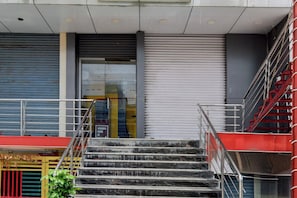 Un conjunto de escaleras de mármol que conducen a la entrada de un edificio con contraventanas cerradas y una escalera roja a la derecha.
