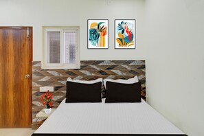 Un dormitorio con una cama, una puerta de madera, un ventanal y dos cuadros abstractos en la pared.