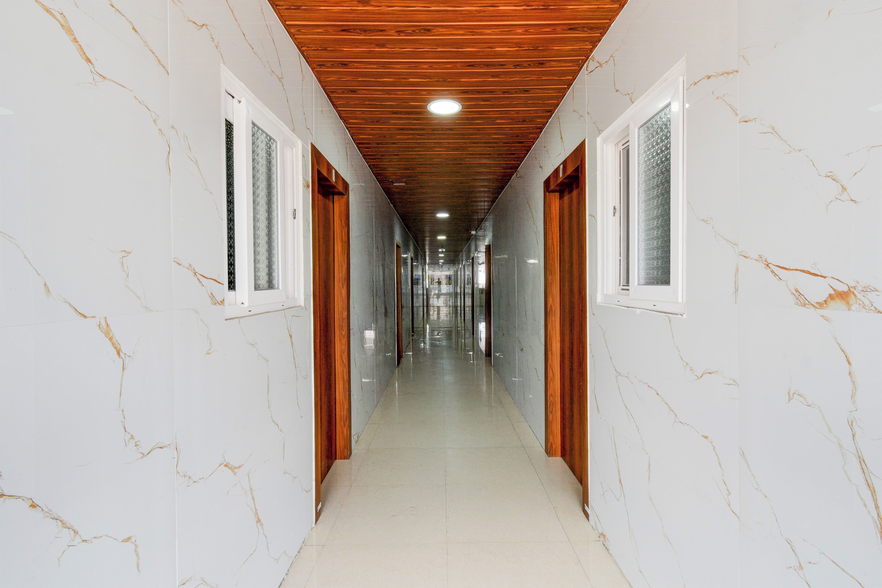 A corridor with white marble walls, wooden doors, and a wooden ceiling.