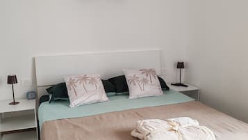 Quarto bem arrumado com cama, travesseiros, mesa de cabeceira com abajur, quadro na parede e piso de madeira.