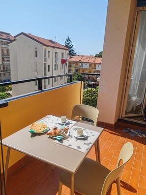 A balcony with a table set for two, including croissants and cups, overlooking a residential area with buildings and a clear sky.
