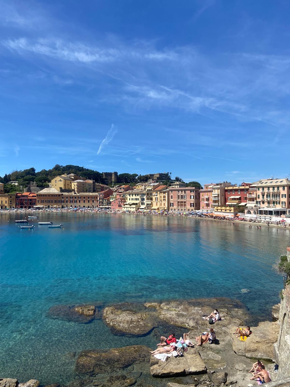 Une ville côtière avec des bâtiments le long du front de mer, une eau d’un bleu limpide et des zones rocheuses où les gens prennent des bains de soleil.