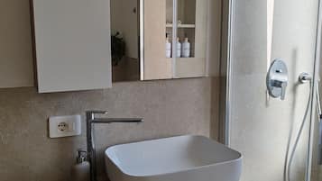 Ein modernes Badezimmer mit einem rechteckigen Waschbecken, einem Spiegel und einer Duschkabine.