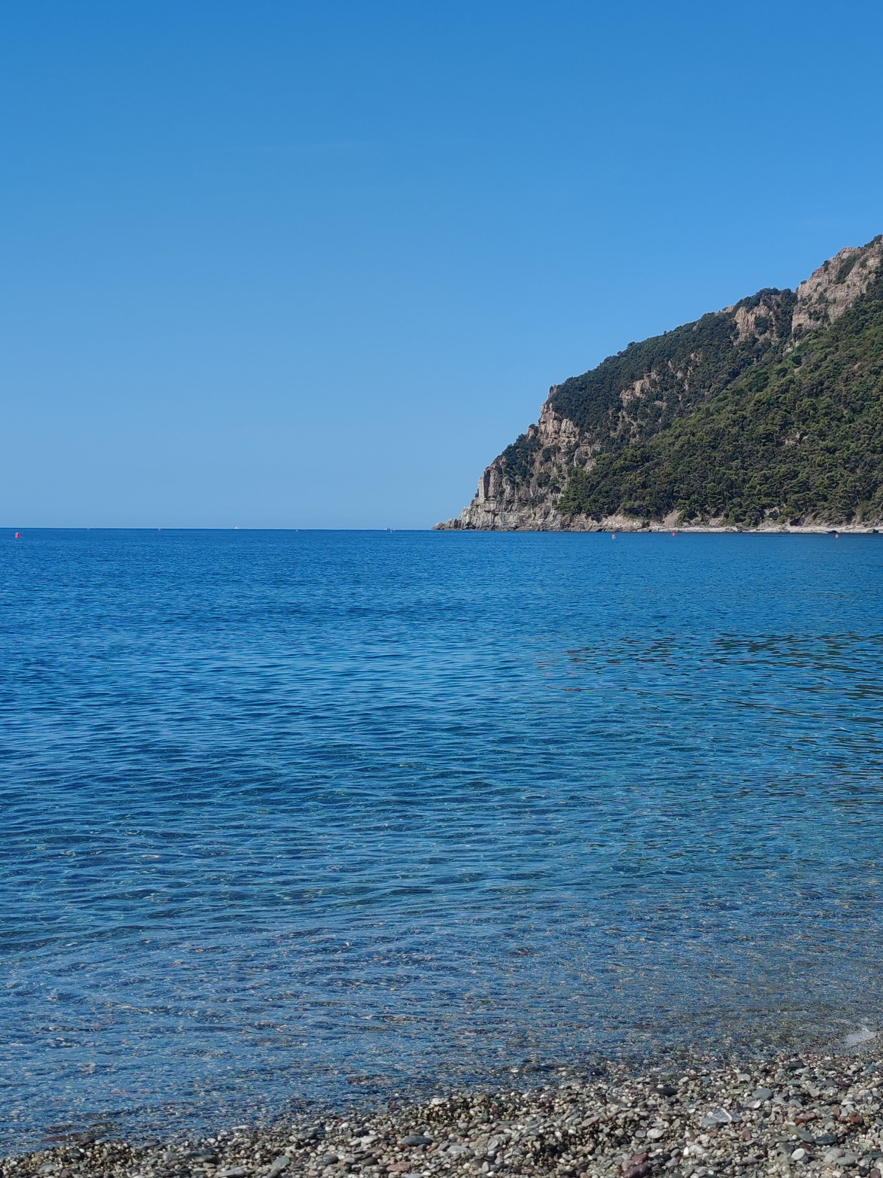 Klares, blaues Meer mit einer felsigen Küste und einem Berg im Hintergrund.
