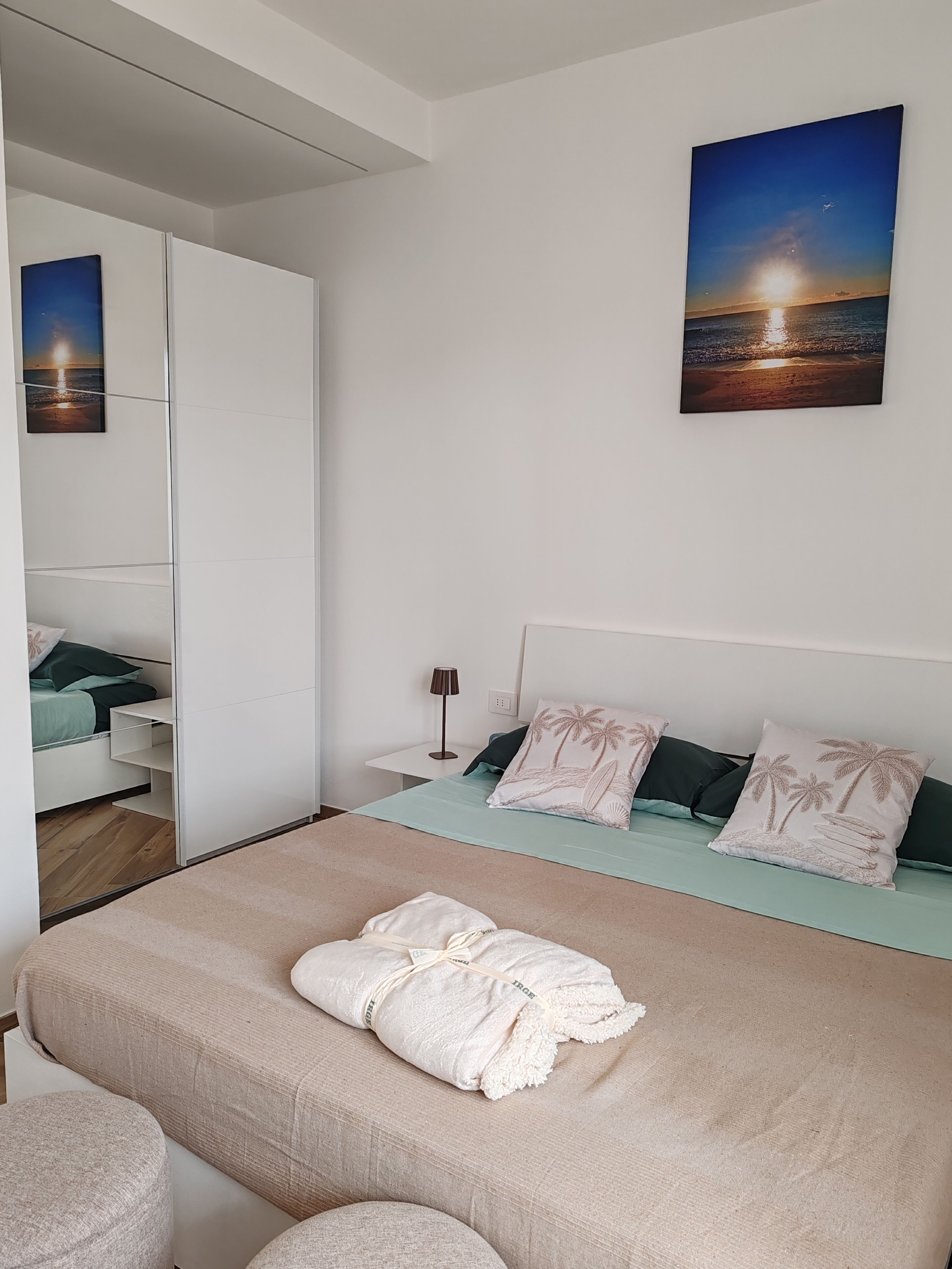Ein Schlafzimmer mit einem Bett, einem Nachttisch, einer Lampe und einem Sonnenuntergangsbild.