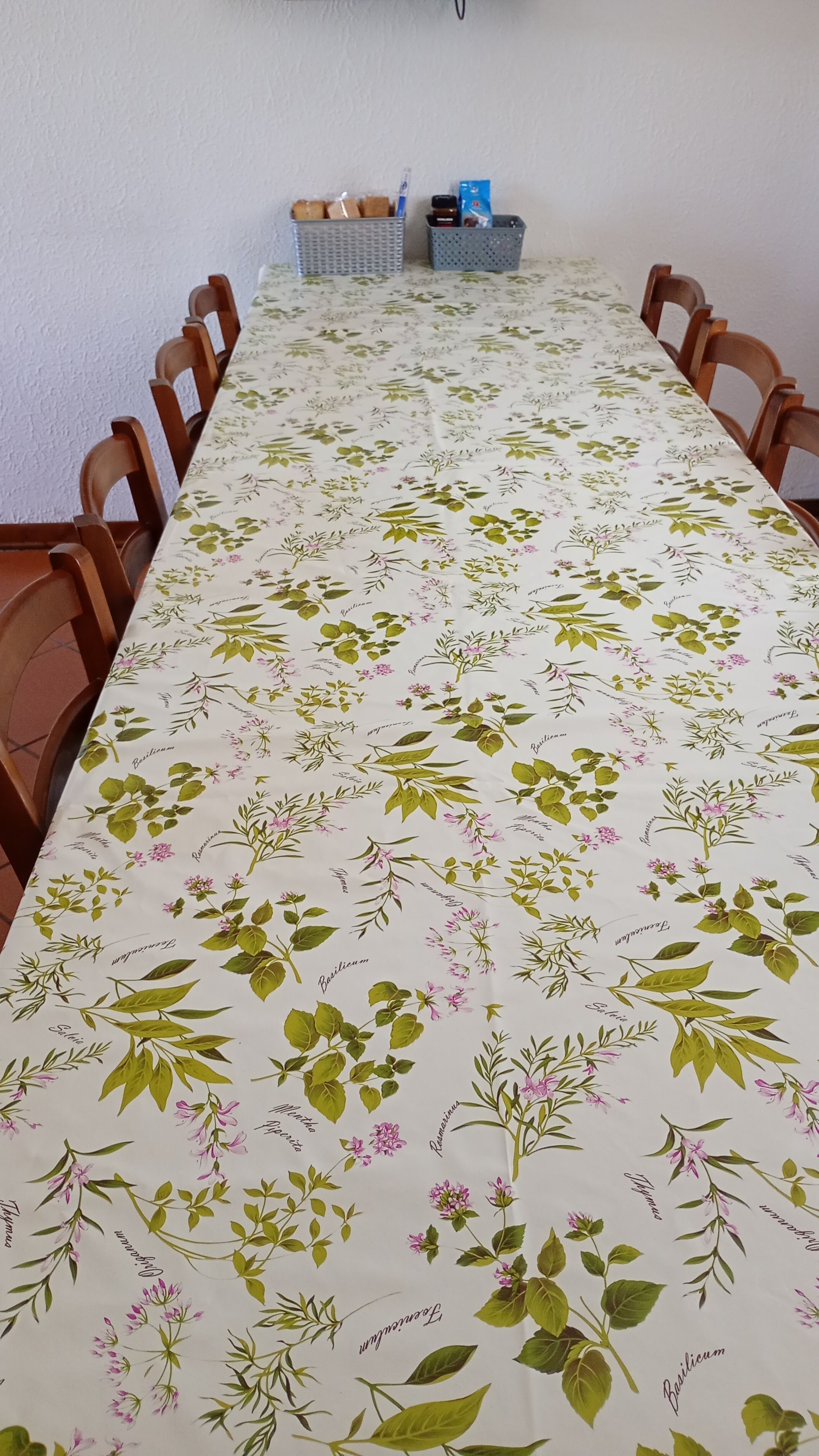 A long dining table with a floral tablecloth, surrounded by wooden chairs.