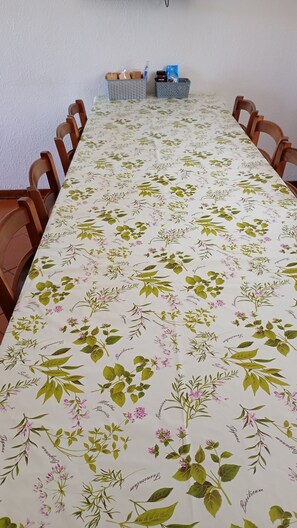 Una taula de dinar llarga amb un mantell floral, envoltada de cadires de fusta.