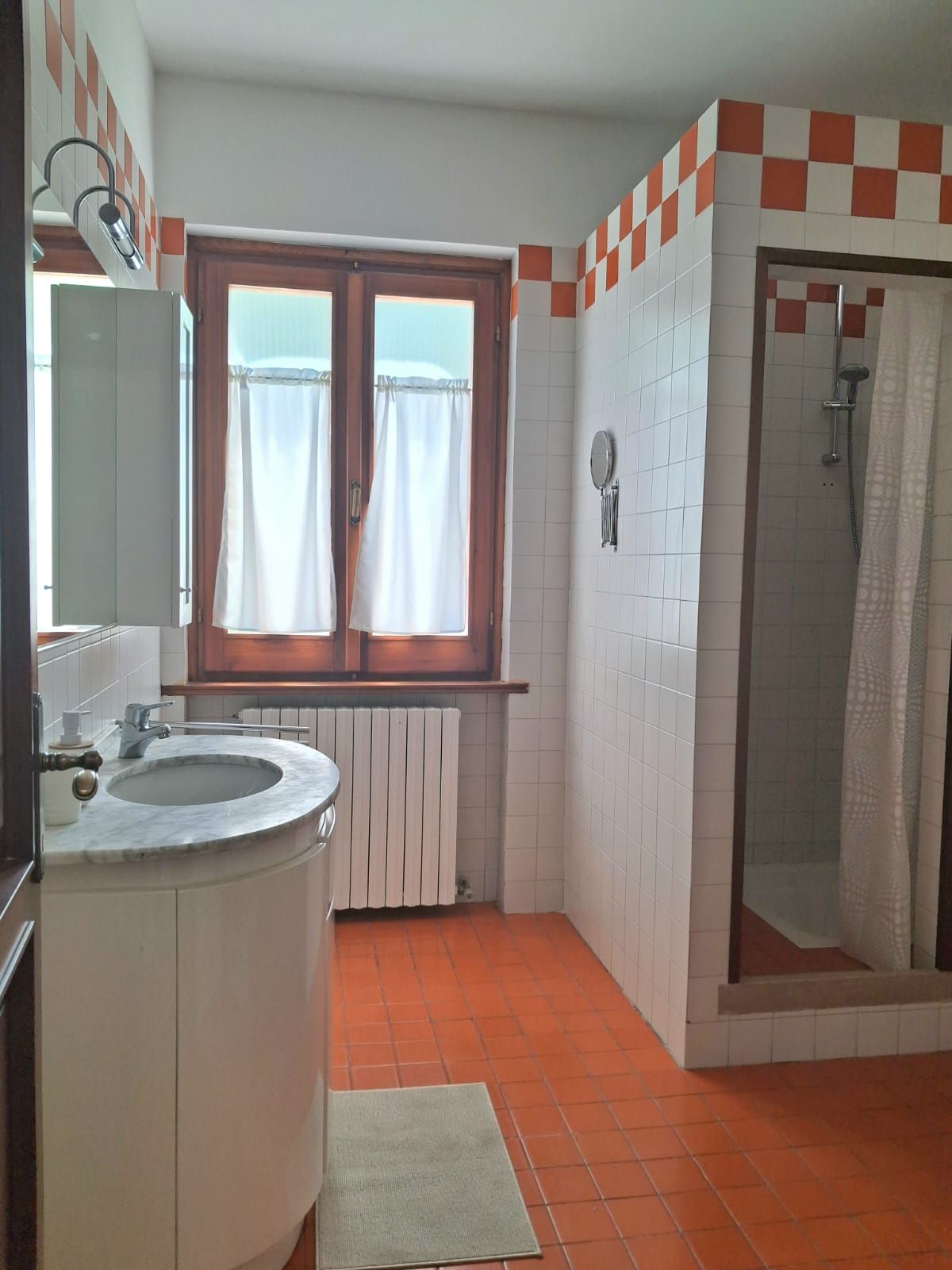 Une salle de bain avec un lavabo, une fenêtre avec des rideaux, une douche et un radiateur.