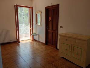 Una habitació amb terra de fusta, un radiador, una porta amb mirall, una taula petita amb una planta i un armari amb detalls verd.