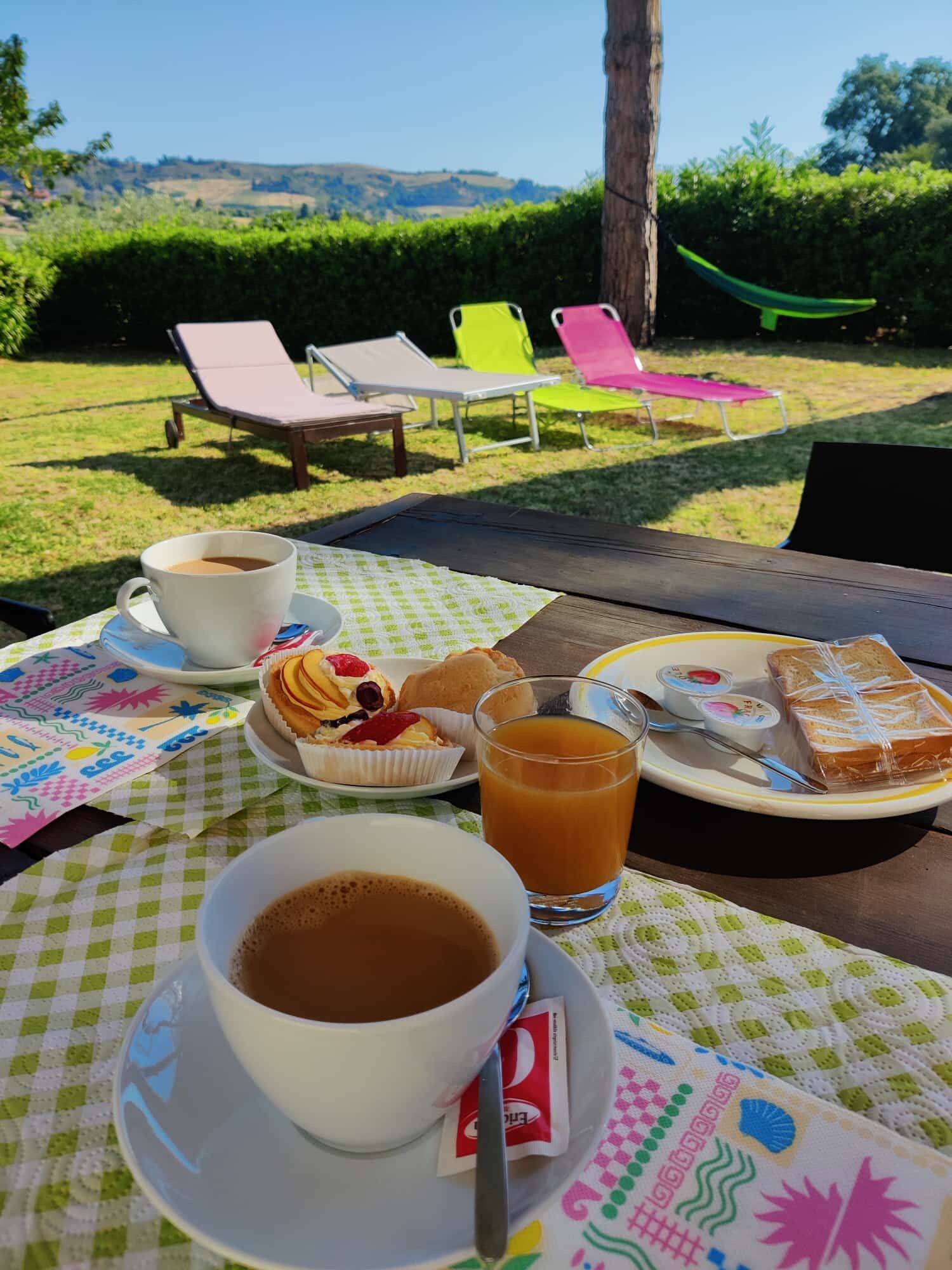 Un tavolo apparecchiato all'aperto con una tazza di caffè, un bicchiere di succo, pasticcini e un piatto di cibo.