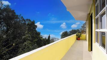 A balcony with a yellow railing, a potted plant, and a clear blue sky with clouds.