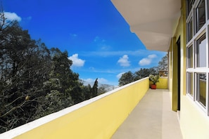 A balcony with a yellow railing, a potted plant, and a clear blue sky with clouds.