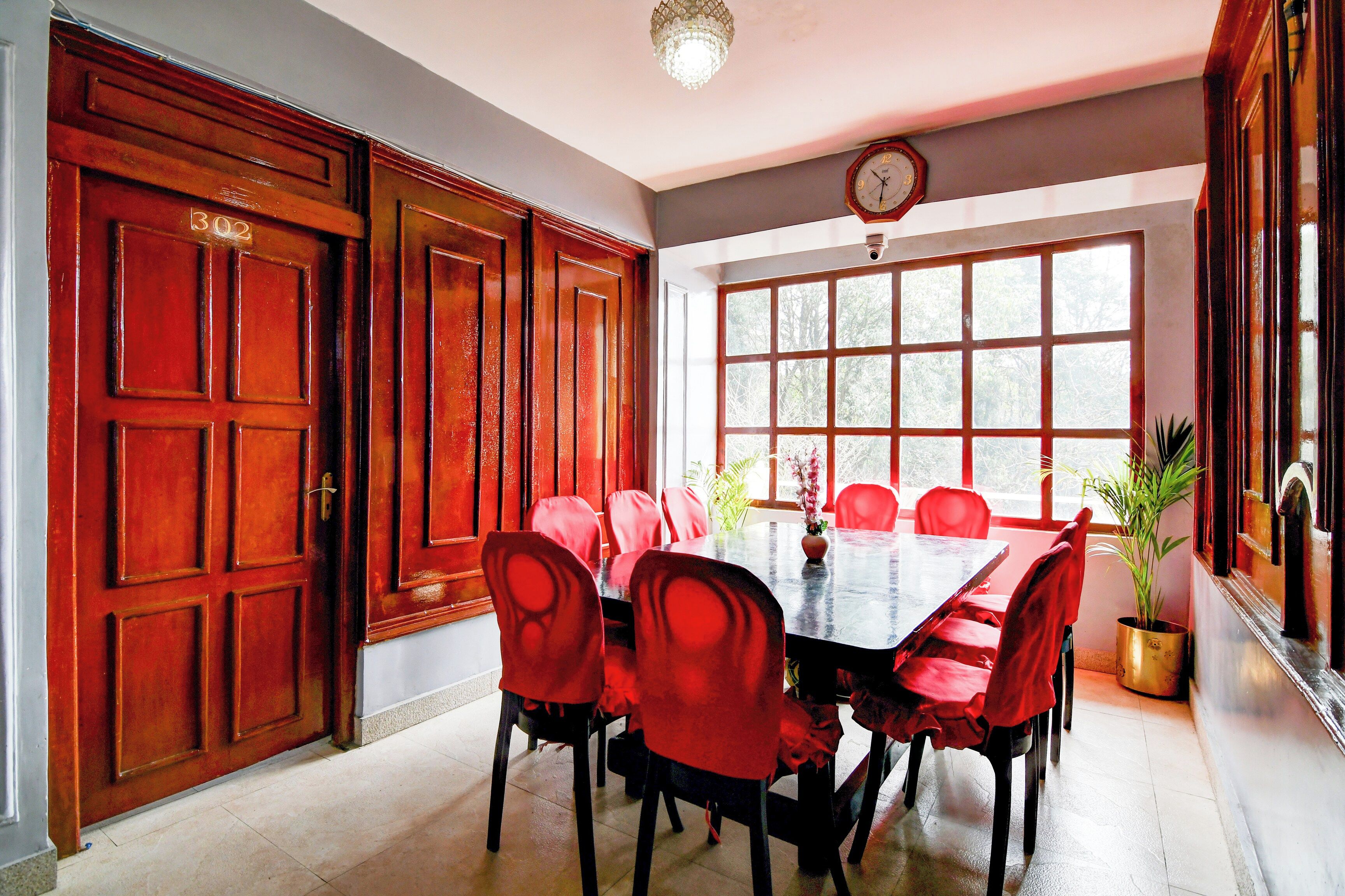 Un espace repas avec une longue table, des chaises rouges et une horloge au mur.