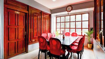 Un espace repas avec une longue table, des chaises rouges et une horloge au mur.