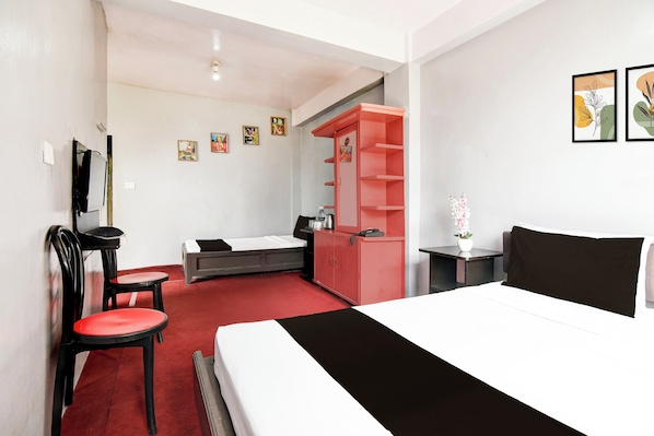Habitación de hotel con cama, escritorio, silla, armario y una pequeña mesa con un jarrón de flores.