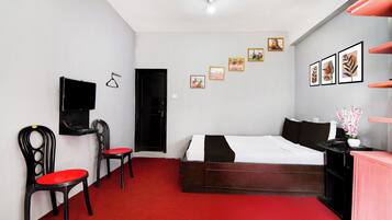 A bedroom with a bed, a desk, a chair, a TV, and a door.