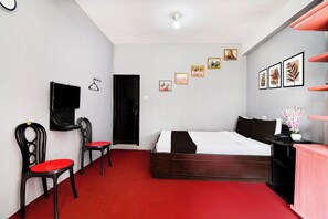 A bedroom with a bed, a desk, a chair, a TV, and a door.