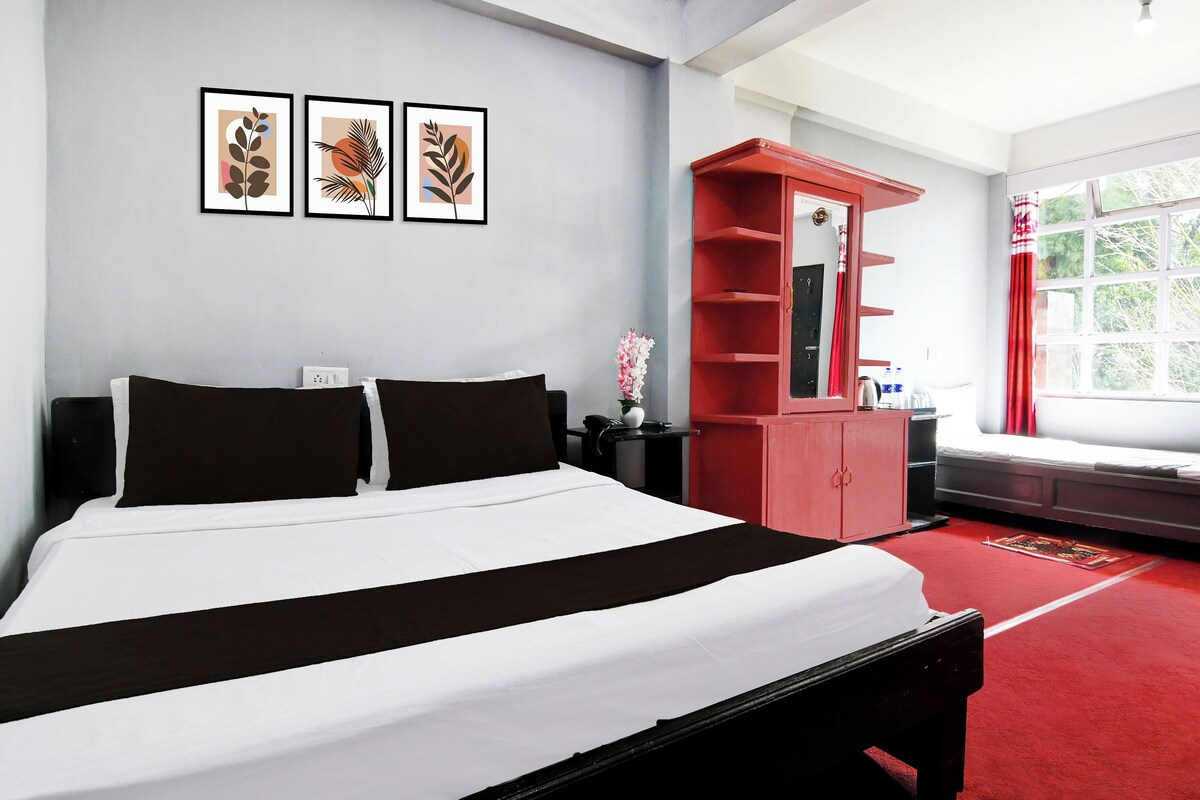 Une chambre d’hôtel avec un lit, une armoire rouge, une fenêtre donnant sur un beau paysage et trois tableaux encadrés accrochés au mur.