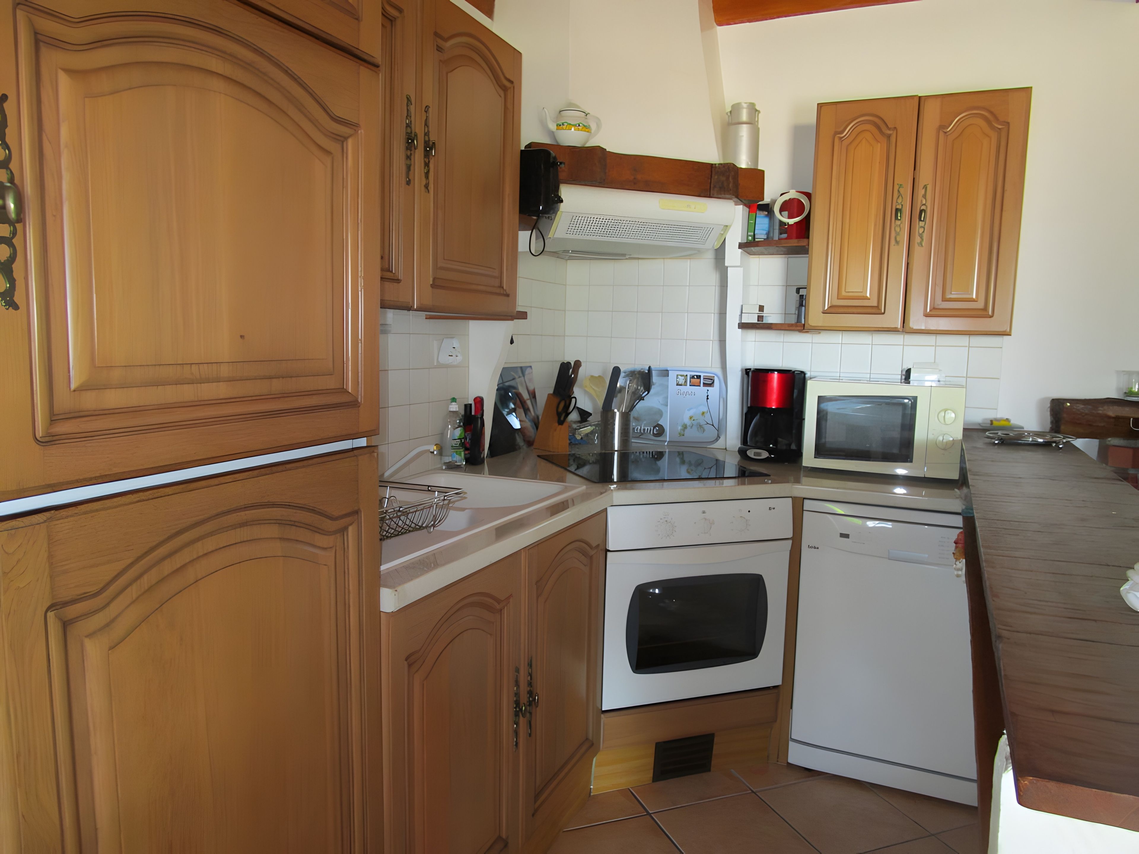 Cocina compacta con armarios de madera, microondas, cafetera y lavavajillas.