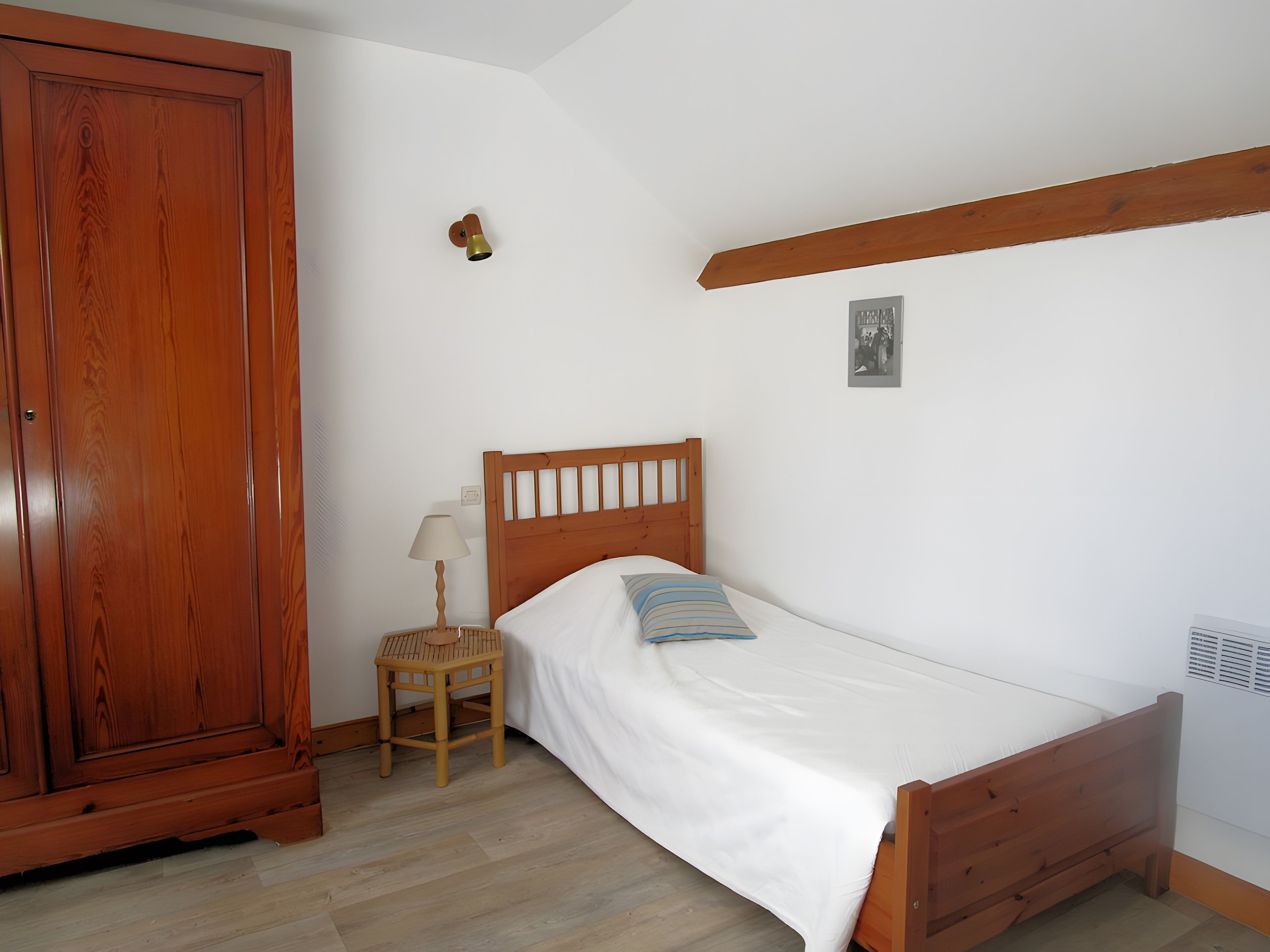 Un dormitorio con una cama de madera, una mesita de noche con lámpara, un armario de madera y una lámpara de pared.