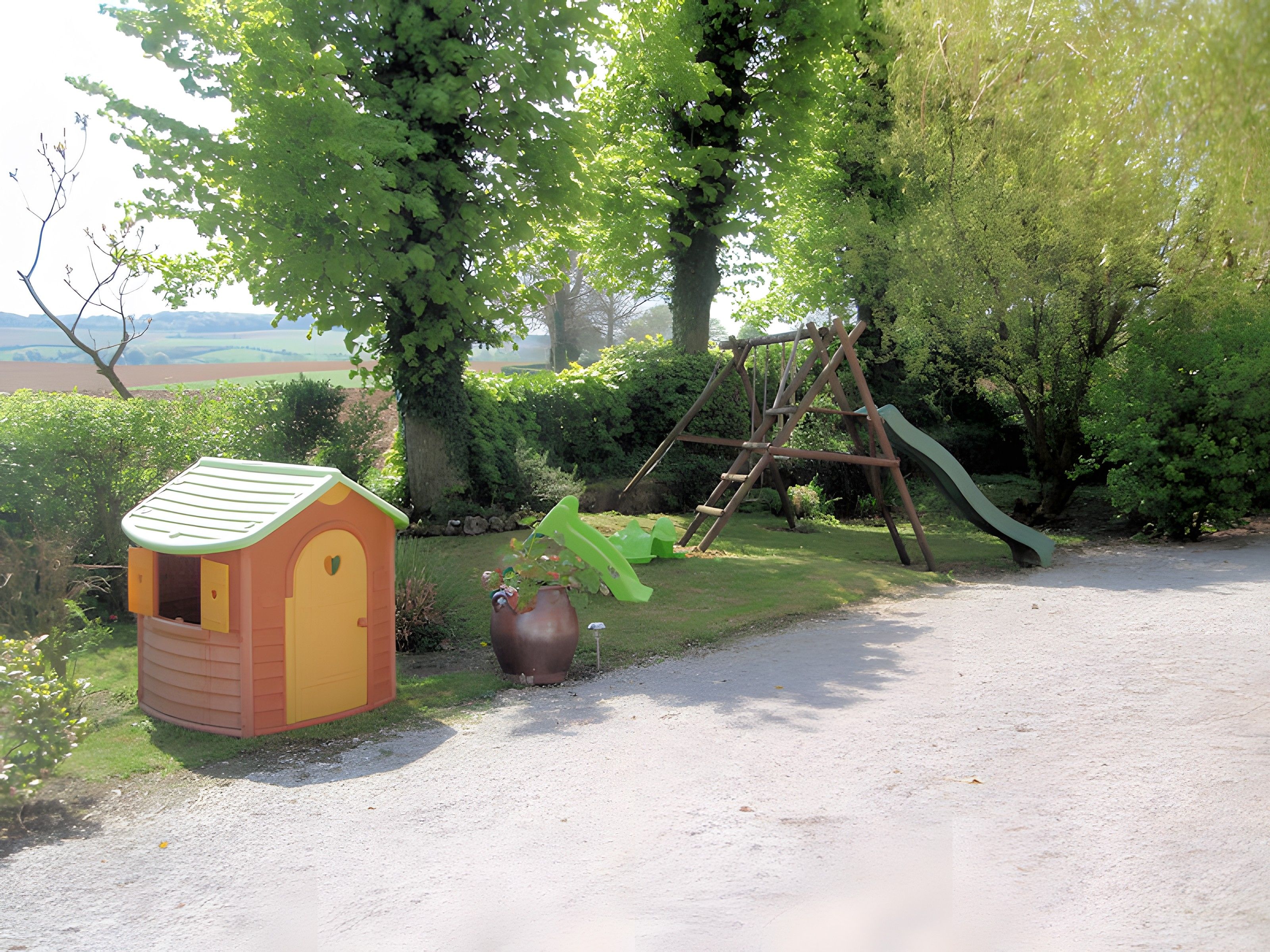 Un jardín con un conjunto de columpios de madera, una casita de juegos y una jardinera grande.