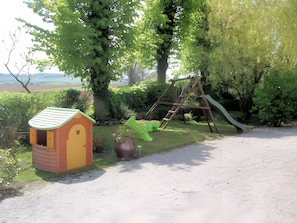 Un jardín con un conjunto de columpios de madera, una casita de juegos y una jardinera grande.