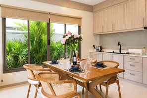 Een moderne keuken met een eettafel voor vier personen, omringd door lichte kastjes en een groot raam met uitzicht op groen.