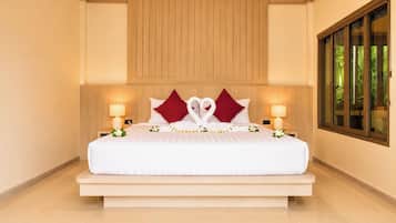 A hotel room with a large bed, two bedside lamps, a wooden headboard, and a window with a view of greenery.