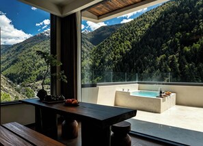 A balcony with a pool, a dining table, and a view of a forested mountain range.
