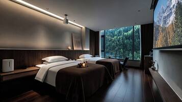 Una habitación de hotel moderna con dos camas, una mesita de noche con lámpara, un ventanal con vistas a un bosque y un cuadro en la pared.