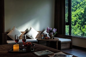 A room with a sofa, a small table with drinks and snacks, a window with a forest view, and a candle.