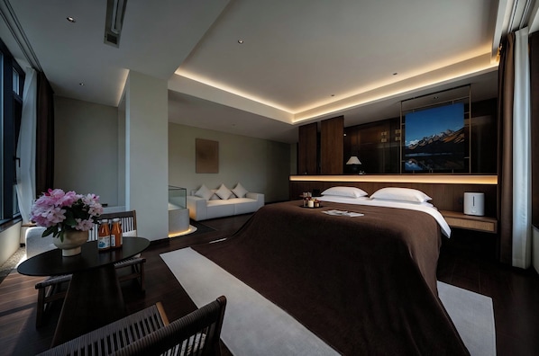 A modern hotel room with a large bed, a desk with a chair, a sofa, and a television.