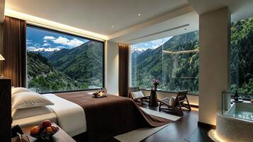 Quarto de hotel moderno com uma cama grande, área de estar com vista para montanhas e uma banheira de hidromassagem com paredes de vidro.