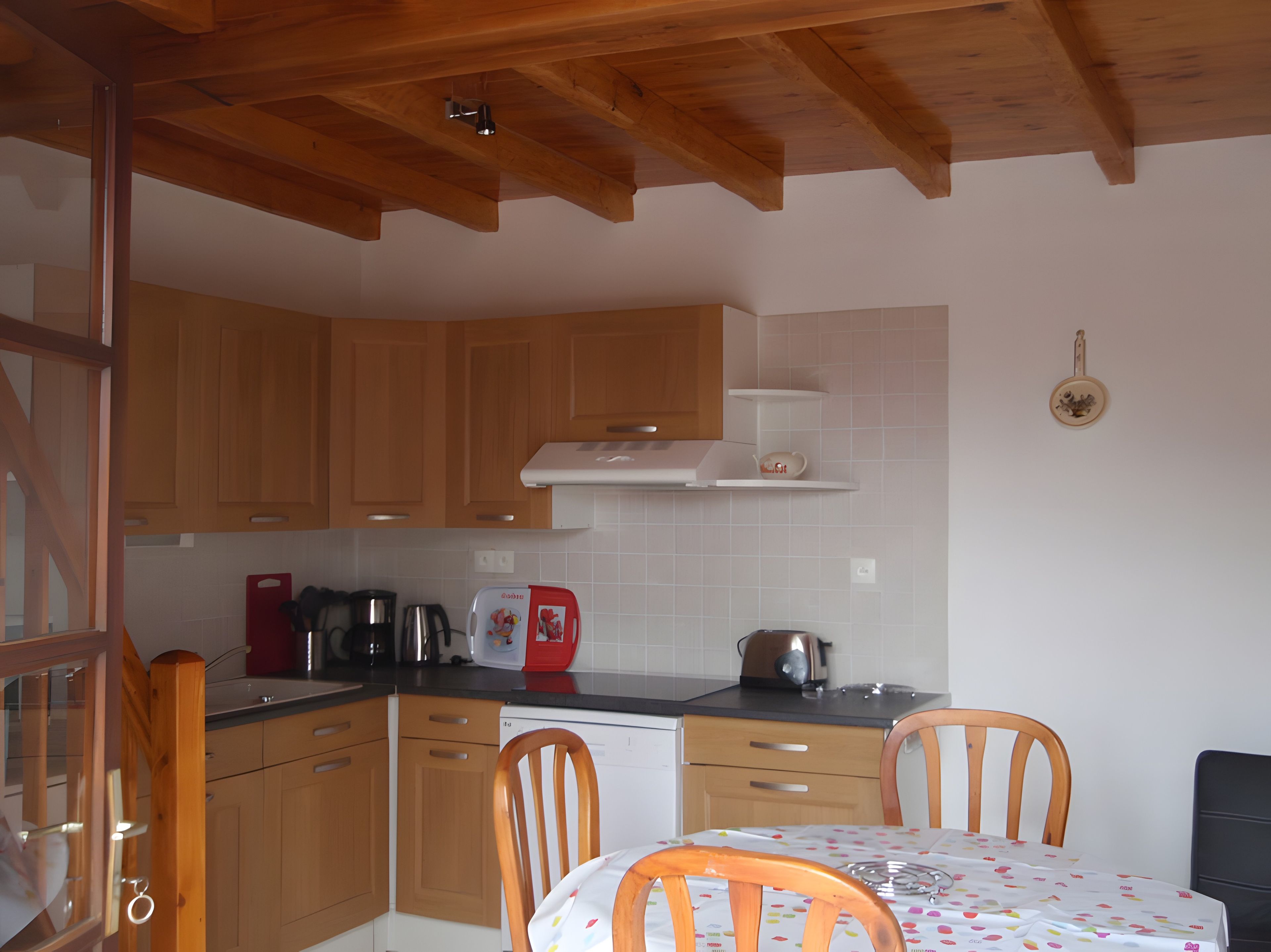 Une cuisine avec des meubles de rangement en bois, une table à manger avec des chaises et une machine à café.
