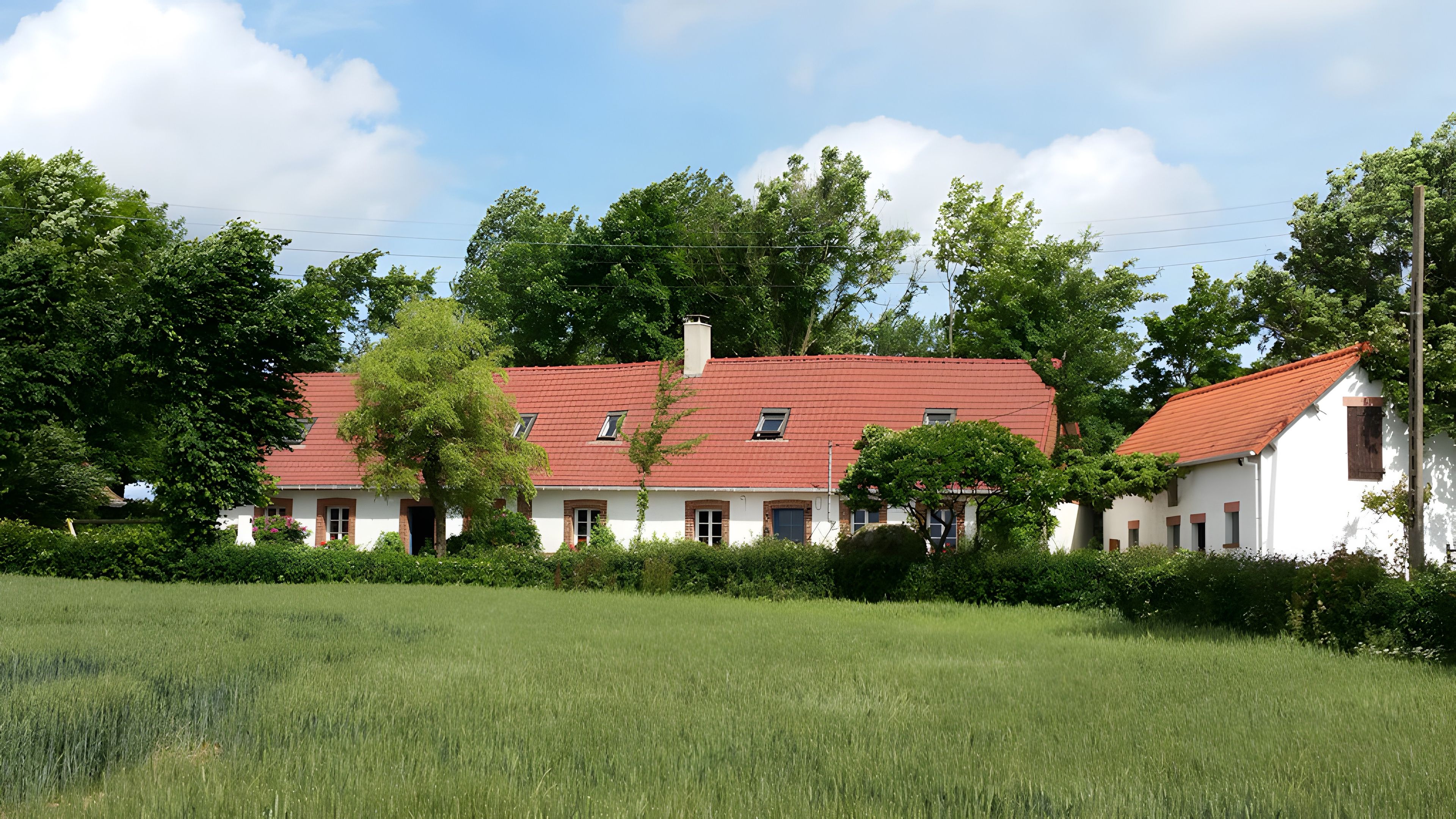 Un bâtiment blanc avec un toit rouge, entouré de verdure et d’arbres.